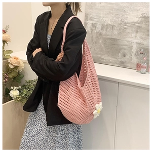 Pink crochet tote bag with a white daisy flower detail shown in a casual summer setting