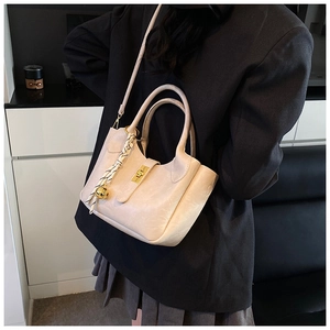 Détail du sac seau plissé crème avec fermoir doré et cloche sur un blazer noir élégant