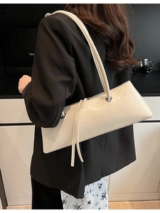 Chic off-white patent leather baguette bag with long strap shown on model's shoulder