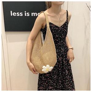 Close-up of a large woven straw tote bag with white flower charm and hollow-out texture