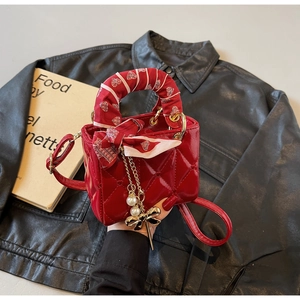 Close-up of red patent leather quilted handbag with pearl charm and silk scarf handle