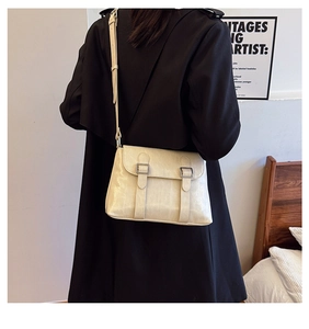 Détail d'un sac bandoulière beige à doubles boucles porté sur un manteau noir