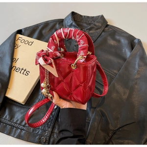 Detail of red quilted handbag with pearl charm and printed silk scarf on handle