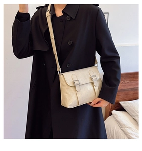Détail d'un sac bandoulière beige clair avec boucles argentées sur un manteau noir