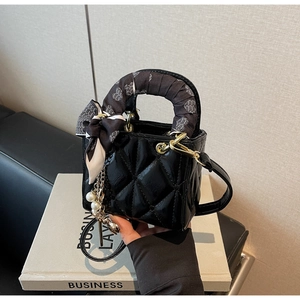 Detail of black quilted patent leather bag with heart scarf and pearl charm accessory