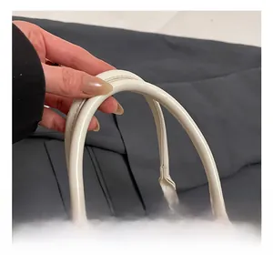 Close-up of a white leather handbag showing its rounded handle and silver metal rings