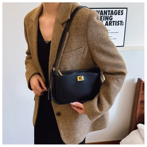 Detail of minimalist black leather shoulder bag featuring a sleek gold metal twist-lock