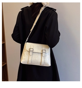 Détail d'un sac bandoulière blanc cassé à doubles boucles porté sur un manteau noir