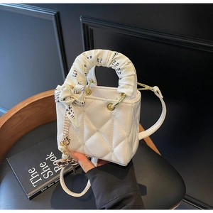 Detail of white quilted handbag featuring silk scarf-wrapped handle and pearl charm pendant