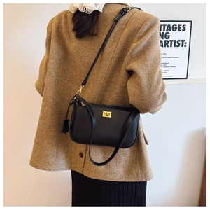 Close-up of black leather crossbody bag with golden square lock on a model