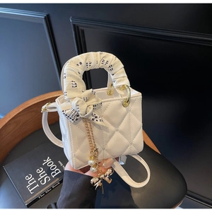 Detail of white quilted mini bag with silk scarf handle and pearl bow charm detail