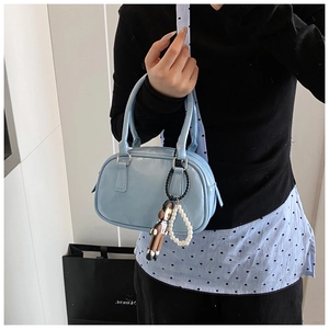Detail of light blue patent leather handbag with a cute monkey charm and pearl strap