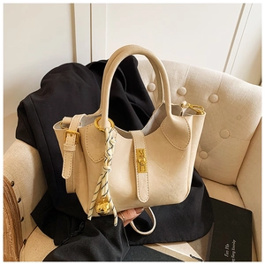 Détail du sac seau en cuir crème avec fermoir rotatif doré et breloque tissée