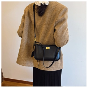 Detail of a chic black leather crossbody bag with a gold square lock on a brown coat