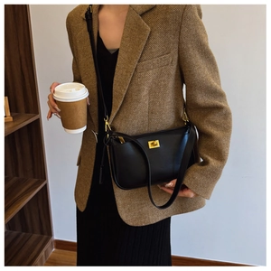 Detail of matte black crossbody bag featuring a decorative gold twist lock and fine strap