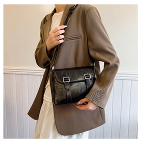Détail d'un sac bandoulière noir en cuir brillant avec deux boucles carrées argentées
