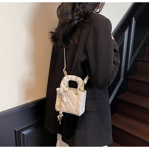 Detail of cream quilted handbag with silk scarf handle and gold chain pendant