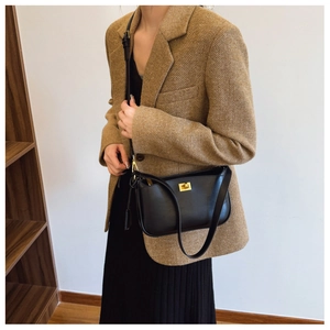 Detail of a black leather handbag with a gold metal twist lock worn by a model