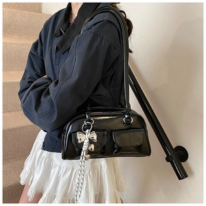 Detalle de bolso de charol negro brillante con colgantes de lazo plateados y bolsillos