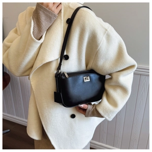 Detailed view of black rectangular crossbody bag with elegant metal twist lock on a beige coat