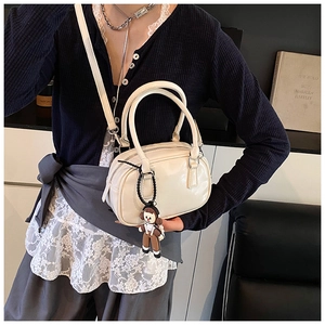 Close-up of off-white mini bowling bag with a cute cartoon doll pendant and adjustable strap