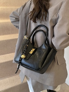 Sac seau noir brillant avec détails dorés et breloque tissée sur mannequin en gris