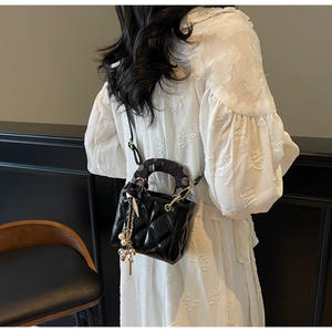 Detail of black glossy quilted mini handbag with silk scarf handle and pearl charm