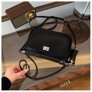 Black leather crossbody bag with silver swivel lock on a vintage wooden counter