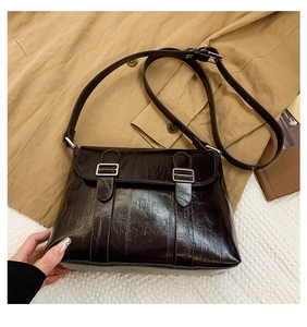 Détail d'un sac bandoulière en cuir marron brillant avec boucles métalliques rétro