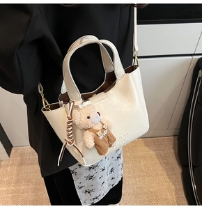 Detail of creamy white leather bucket bag with plush bear charm and embossed logo