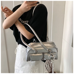 Detalle del bolso Boston plateado con bolsillos frontales dobles y colgante de lazo metálico