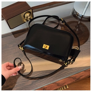 Close-up of black leather crossbody bag with golden square metal lock on a table