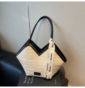 Detail of beige woven straw tote with black leather trim and V-shaped opening design