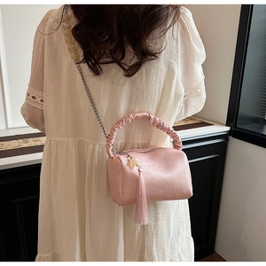 Close-up of pink cylindrical crossbody bag featuring pleated handle and long fringe tassel