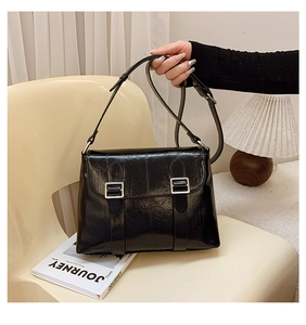 Détail du sac à main en cuir noir brillant avec boucles argentées et bandoulière