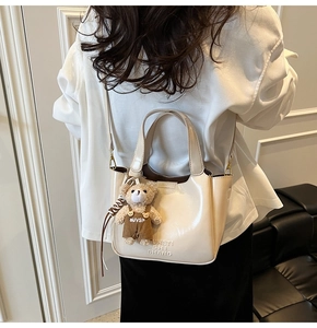 Detail of cream PU leather bucket bag with embossed text and cute brown bear pendant