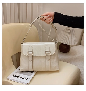 Détail d'un sac messager vintage blanc crème avec boucles en métal argenté sur chaise