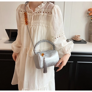 Silver cylinder bag featuring metallic patterns, chain strap, and elegant tassels