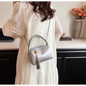 Detail of silver pleated pillow bag showing ruched handle, metal chain, and tassel accents