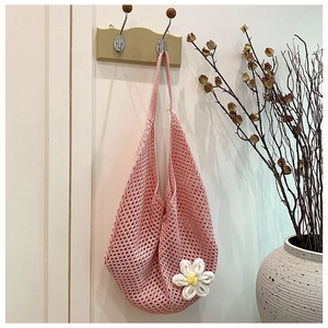 Detailed close-up of pink crochet knit tote bag with 3D white floral accent on wood hook