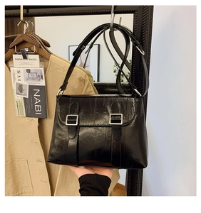 Détail du sac bandoulière en cuir noir avec texture vintage et doubles boucles argentées