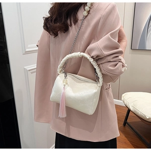 Close-up of white embossed leather bag with pleated handle, pearl chain, and pink tassel charm