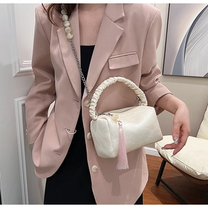 Detail of cream leather pillow bag with pleated handle, pearl chain, and pink tassel