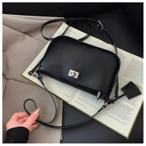 Close-up of minimalist black matte crossbody bag with silver rotating lock on a book