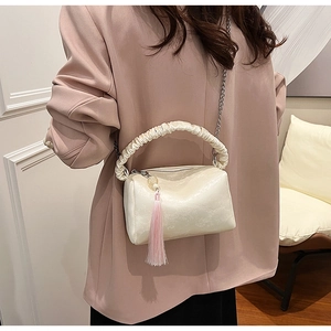 Detail of creamy white pleated pillow bag featuring a silver chain and pink tassel charm