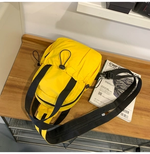 Top view of bright yellow tactical crossbody bag with black straps on a wooden surface