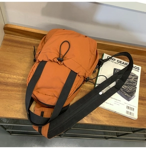 Close-up of orange tactical crossbody bag with drawstring pocket on a wooden surface