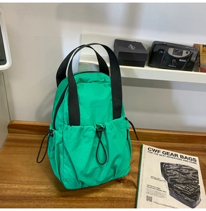 Detail view of bright green nylon backpack with drawstring pockets and black handles