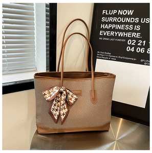 Close-up of brown woven tote bag featuring leather handles and houndscotth scarf detail