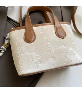 Detail of cream bucket bag with star embossed pattern and brown leather trim accents